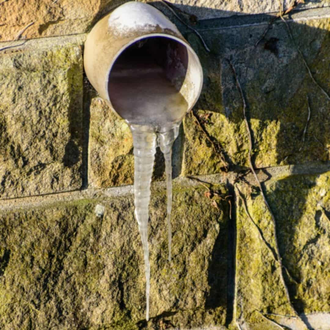 Icicles hanging from a pipe on an exterior stone wall