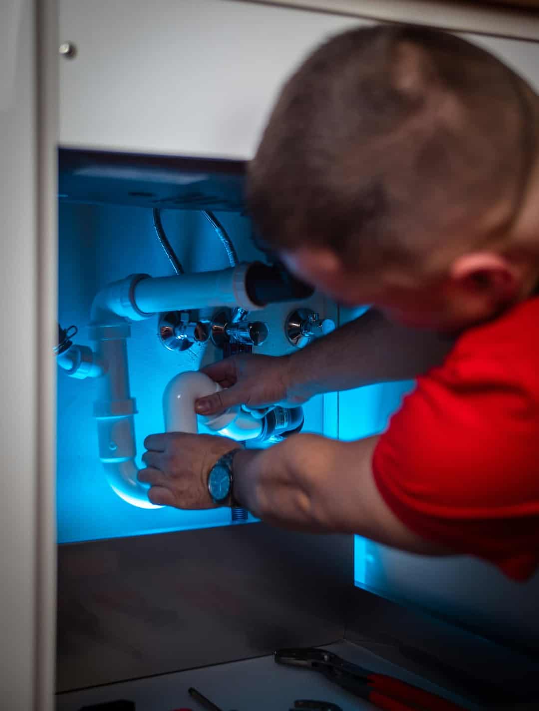 Plumber reconnecting drain pipes under a sink