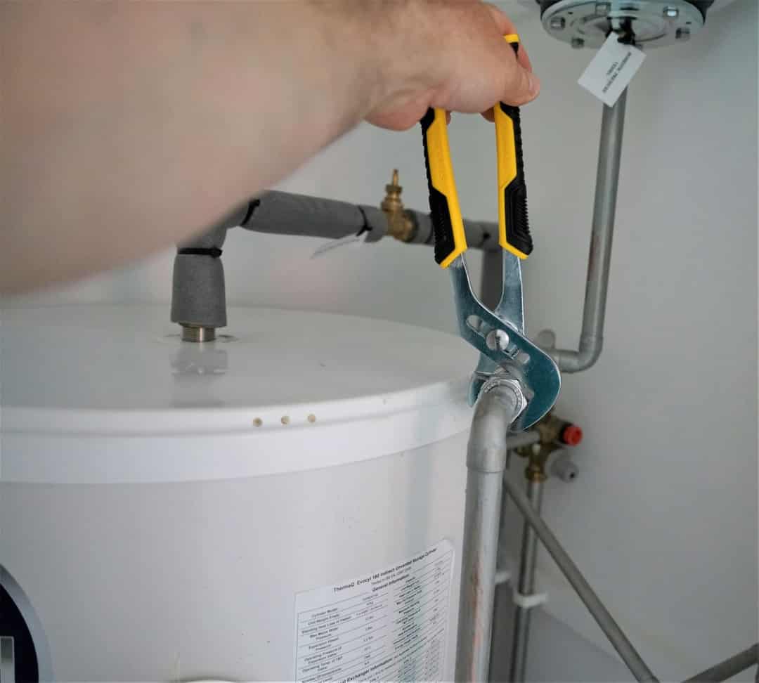 Pliers tightening a pipe fitting on top of a water heater