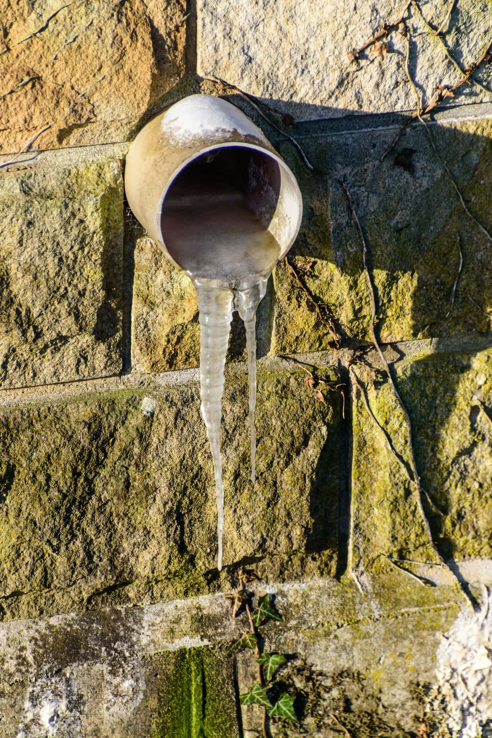 Icicles hanging from a pipe on an exterior stone wall