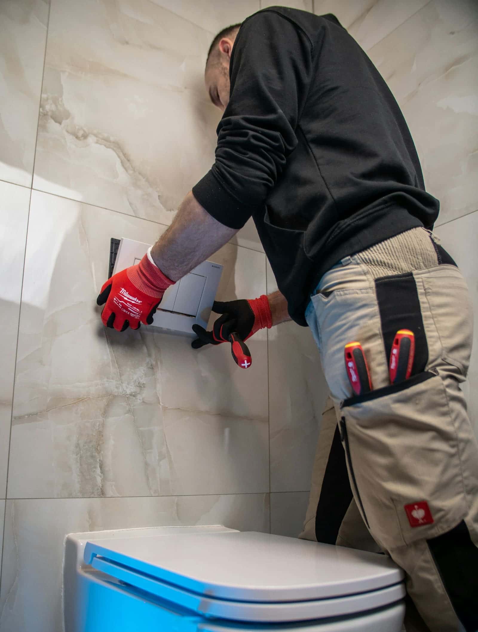 Plumber in red work gloves working on the wall behind a toilet