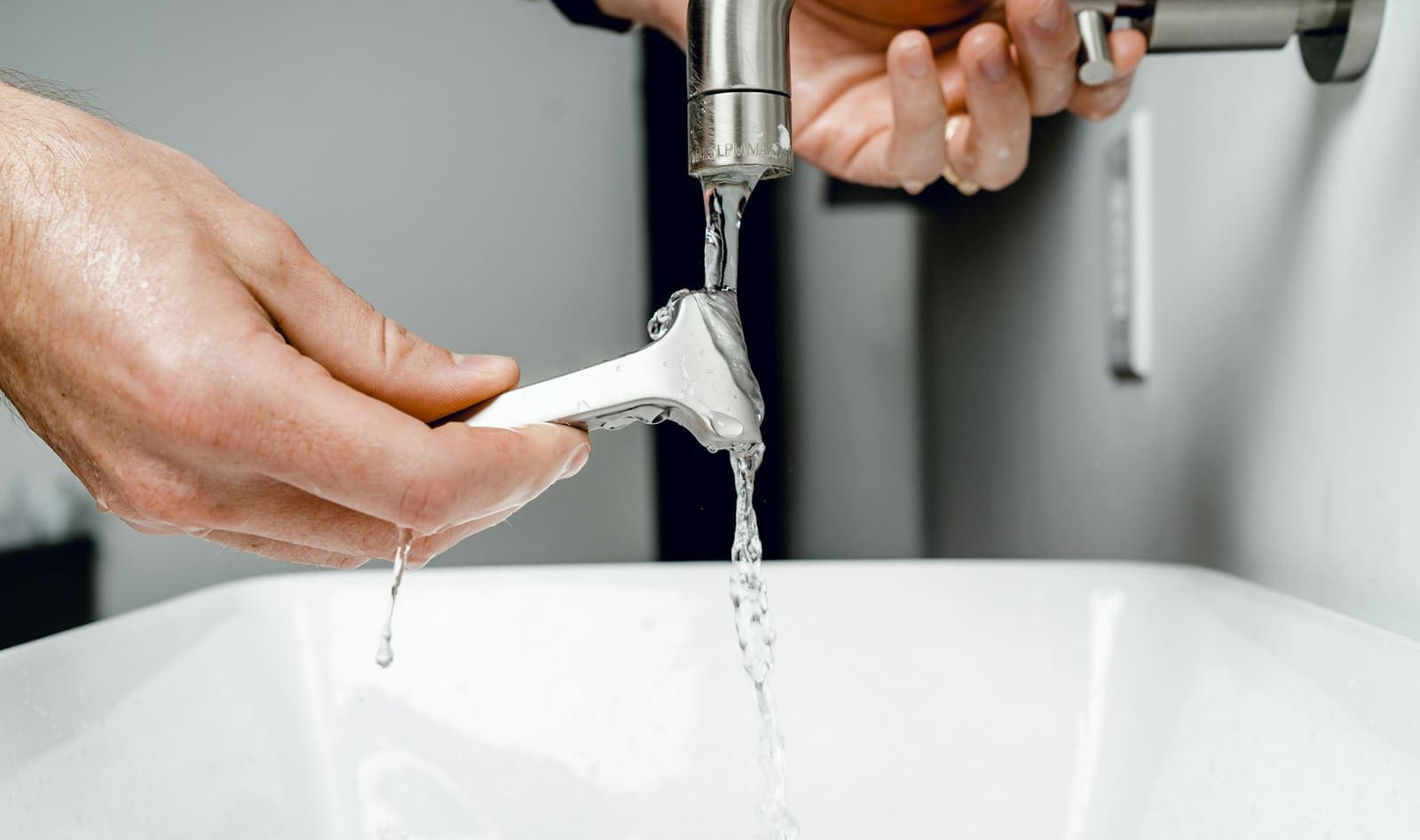 Hand under a running chrome bathroom faucet