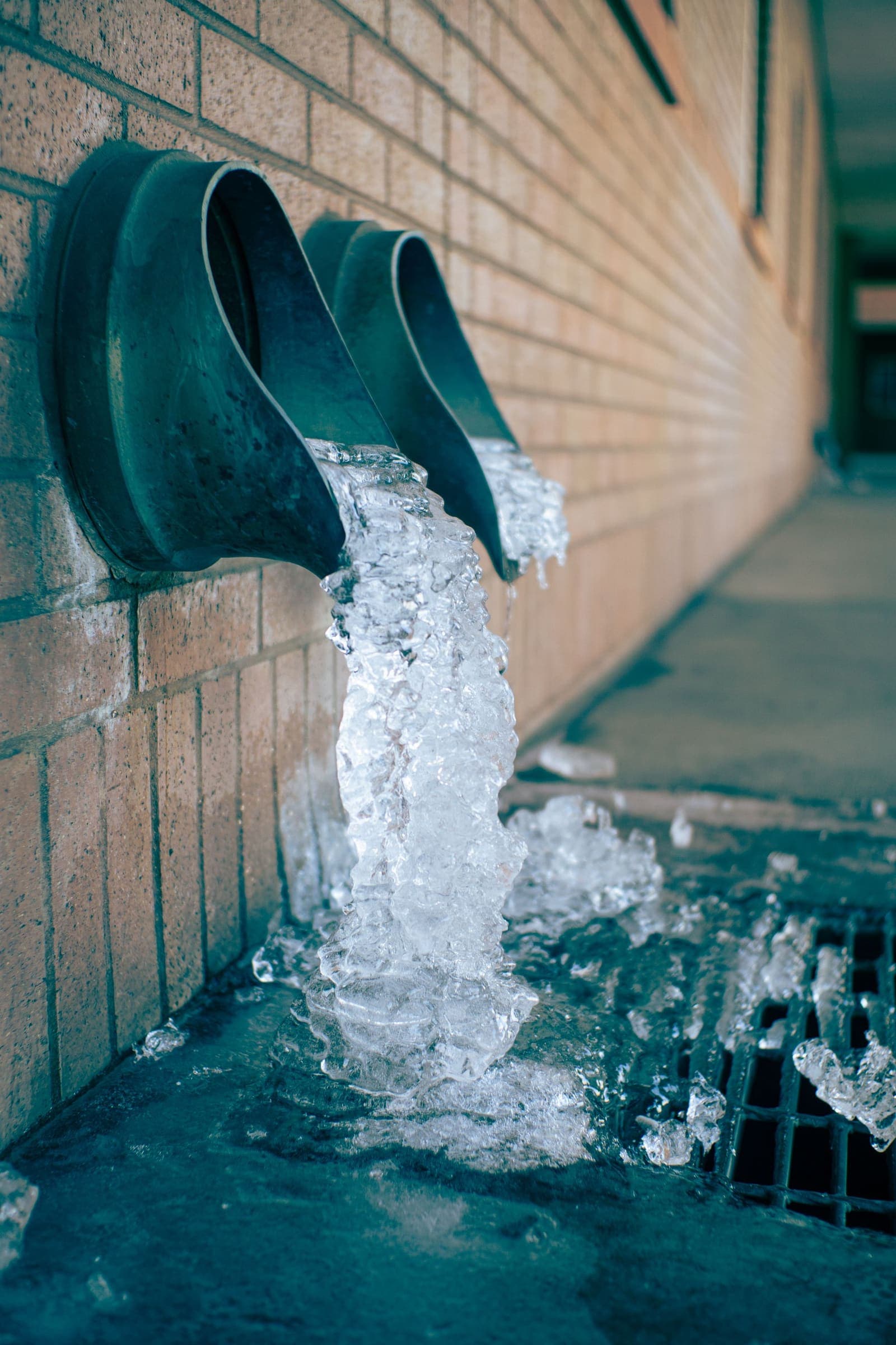 Ice spilling from a frozen drain pipe into a grate