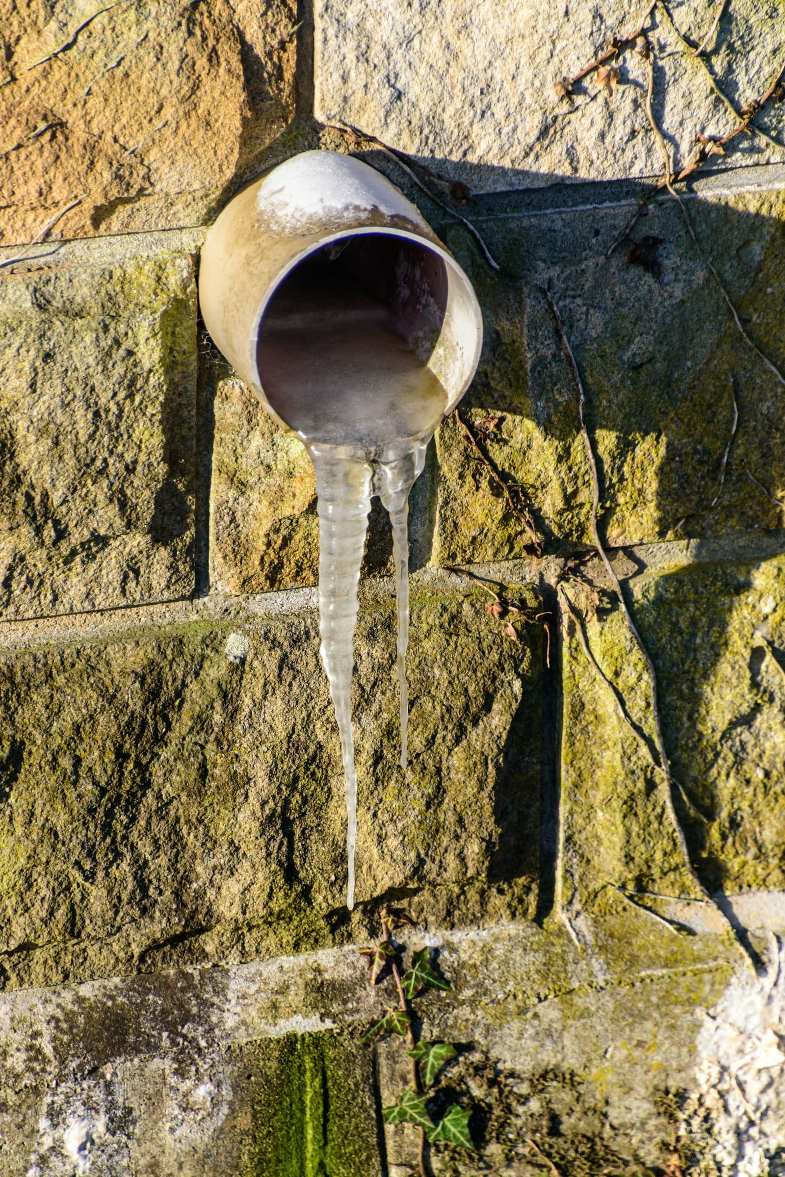 Icicles hanging from a pipe on an exterior stone wall