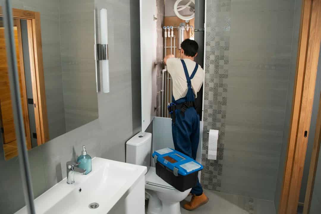 Plumber with a toolbox working in a small bathroom