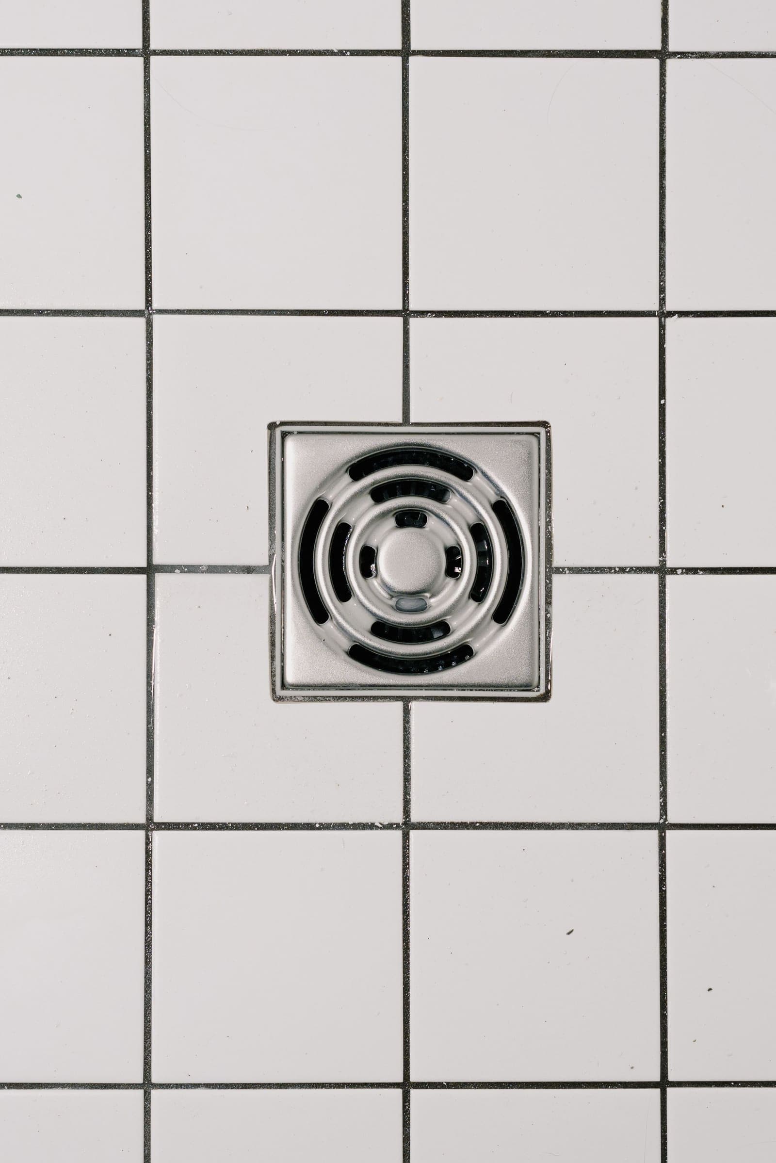 Square stainless steel shower floor drain in white tile