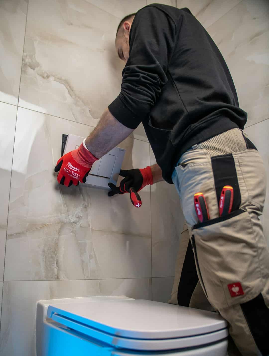 Plumber in red work gloves working on the wall behind a toilet