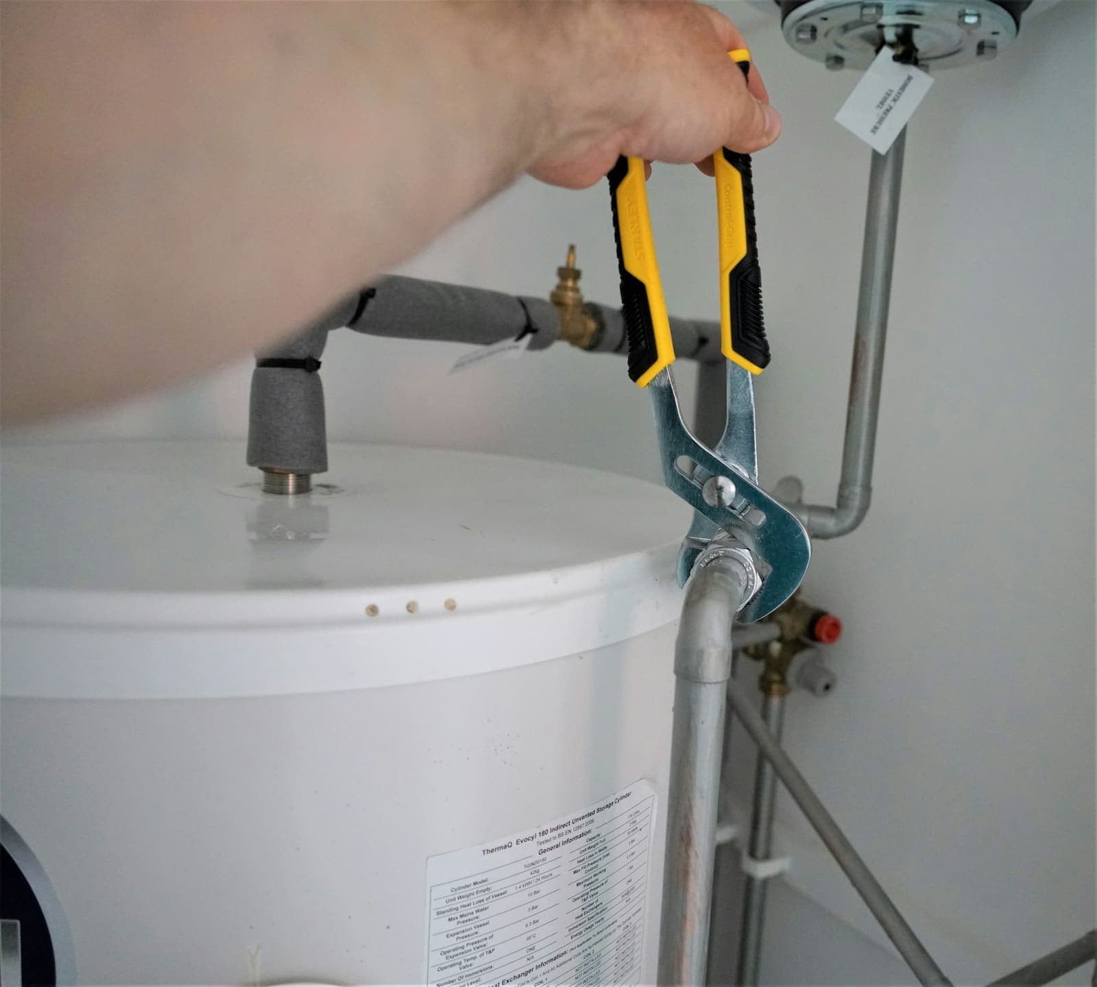 Pliers tightening a pipe fitting on top of a water heater